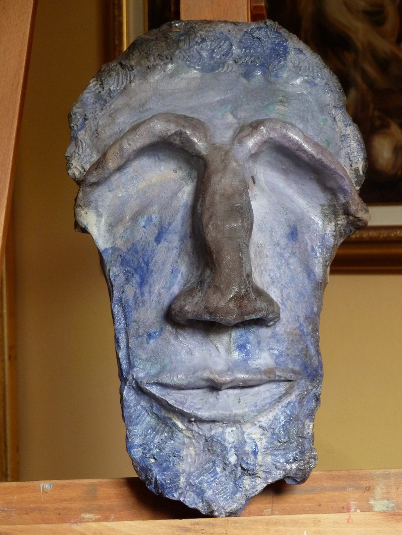 Maschera in argilla raku con forma allungata, texture materica e colorazioni blu-grigie, simbolo di introspezione ed essenzialità.